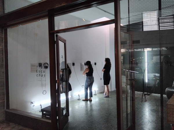 Three people listening on headphones, pictured from outside the gallery