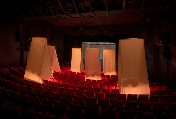 An overview of the auditorium with low-lit tent-like structures hanging from the ceiling over some of the seats